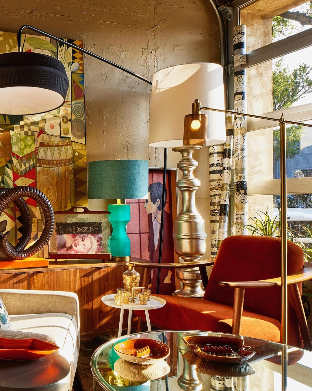 Interior view with a vintage modern style living room with an orange chair, lamps, and decorative objects. Artwork is visible on the wall.