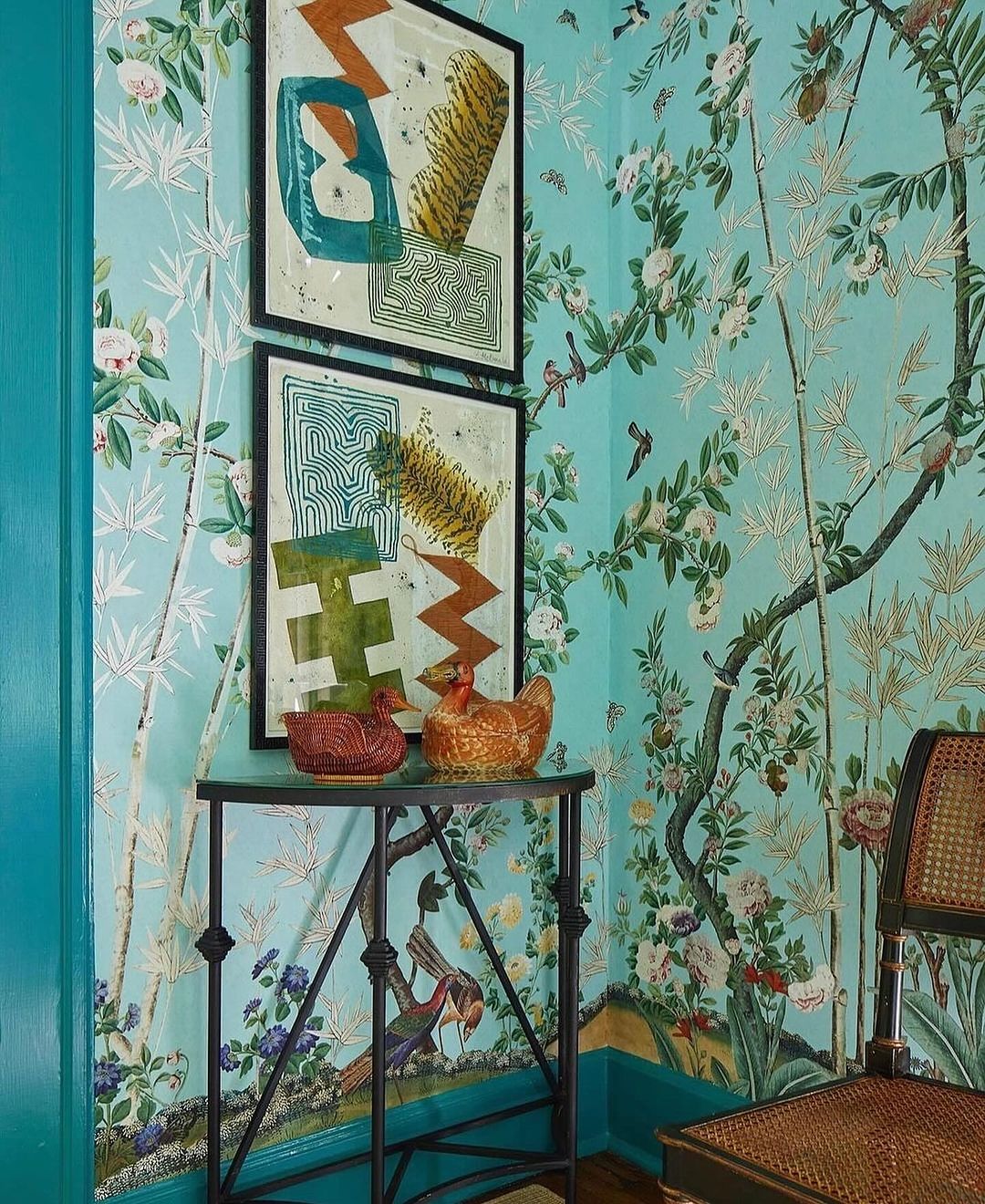 Whimsical interior featuring two prints above a small table with decorative hen figures against a vibrant floral patterned wall.