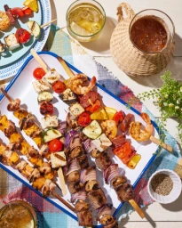 Overhead food photography of grilled skewers with shrimp, vegetables, and meat on a white enamel tray