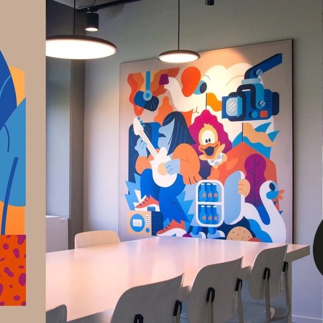 Wide interior view of an office space featuring a large colorful cartoon illustration and a long white conference table surrounded by chairs.