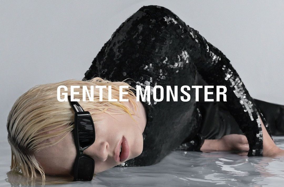 Fashion shot of an adult woman with light blonde hair wearing black sunglasses and a shiny black sequin jacket laying in water.
