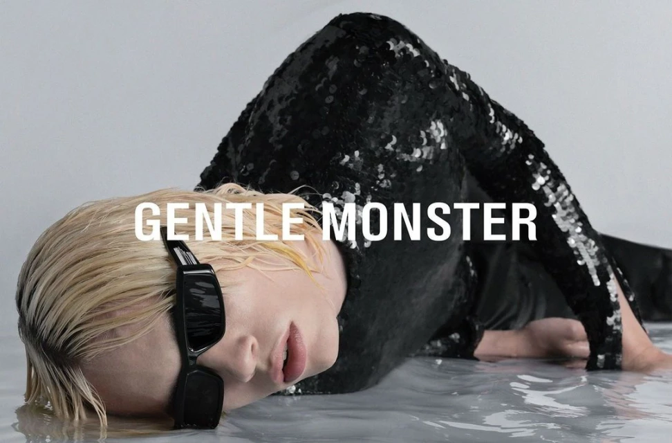 Fashion shot of an adult woman with light blonde hair wearing black sunglasses and a shiny black sequin jacket laying in water.