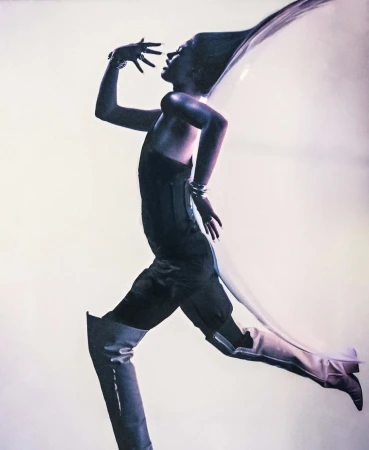 Model in profile wearing a dark outfit and tall boots striking a dynamic running pose against a light gradient background.