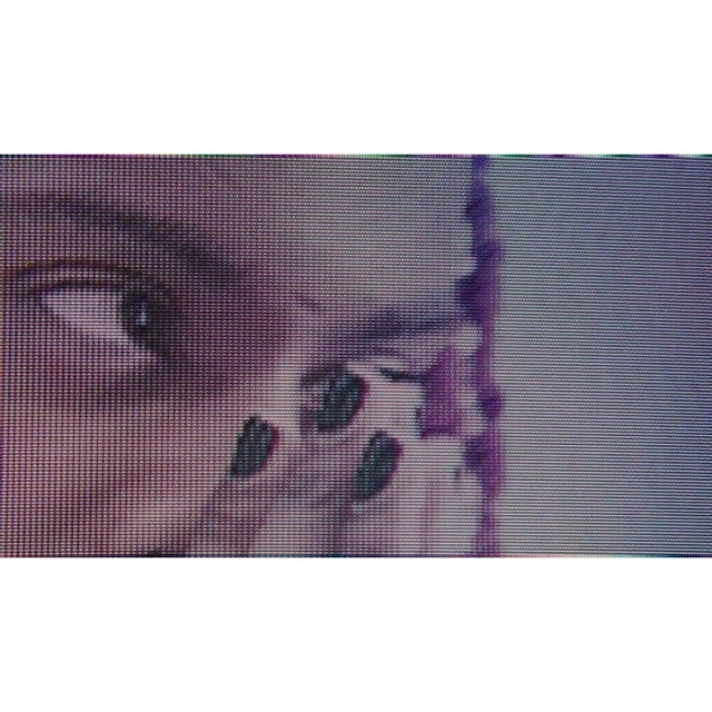 Close-up of a person's face partially visible with braided hair. The image shows the eye, parts of the cheek, and fingernails with dark polish.