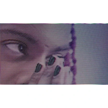 Close-up of a person's face partially visible with braided hair. The image shows the eye, parts of the cheek, and fingernails with dark polish.