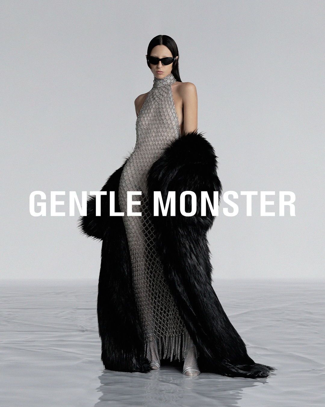 Fashion shot: A woman in a silver gown and black fur coat poses in a studio with 'GENTLE MONSTER' text overlay.