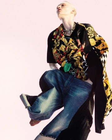 Model in low angle shot wearing patterned black and yellow top and loose blue denim jeans against a pale background