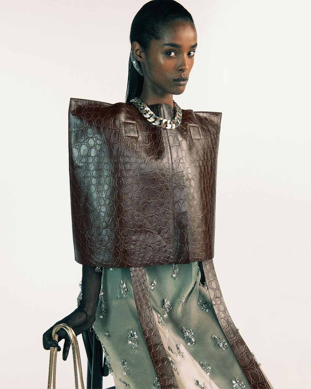 Elegant woman in a brown faux-crocodile top and necklace, posing in a studio with a white background, fashionable and chic.