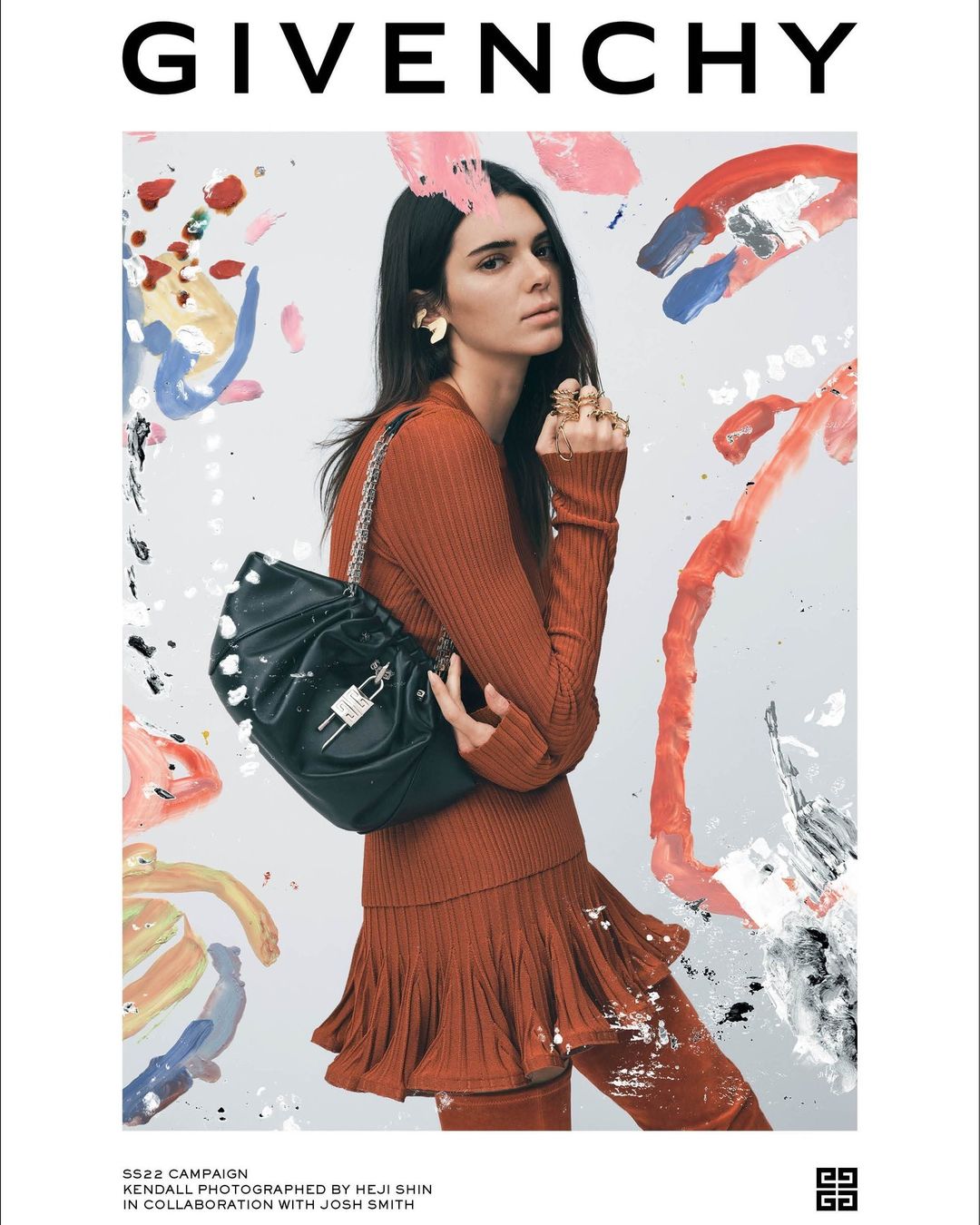 Kendall Jenner poses in a rust-colored outfit with a Givenchy bag against a painterly backdrop, showcasing fashion and style.