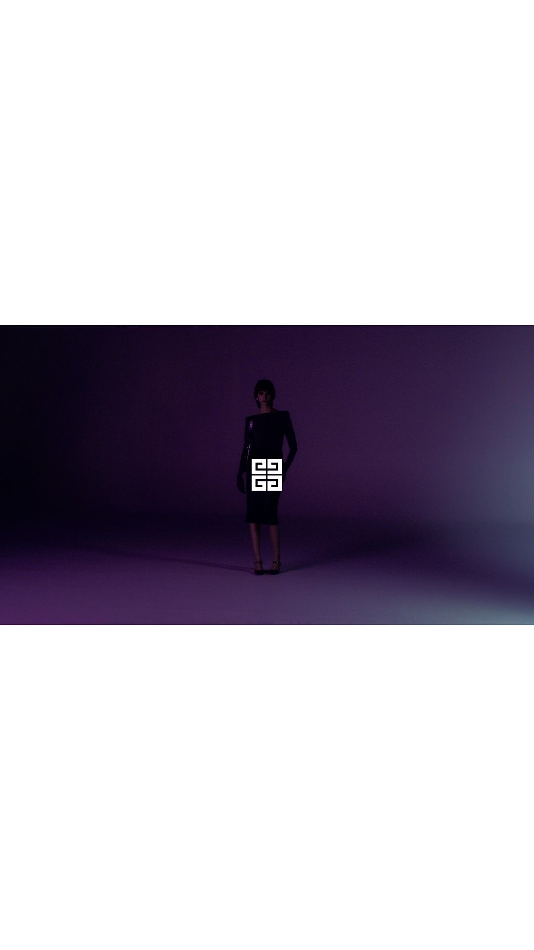 Adult woman in dark dress and shoes in a dimly lit purple studio, branded with a large, white Givenchy logo on the dress.