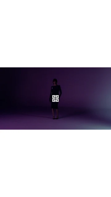 Adult woman in dark dress and shoes in a dimly lit purple studio, branded with a large, white Givenchy logo on the dress.