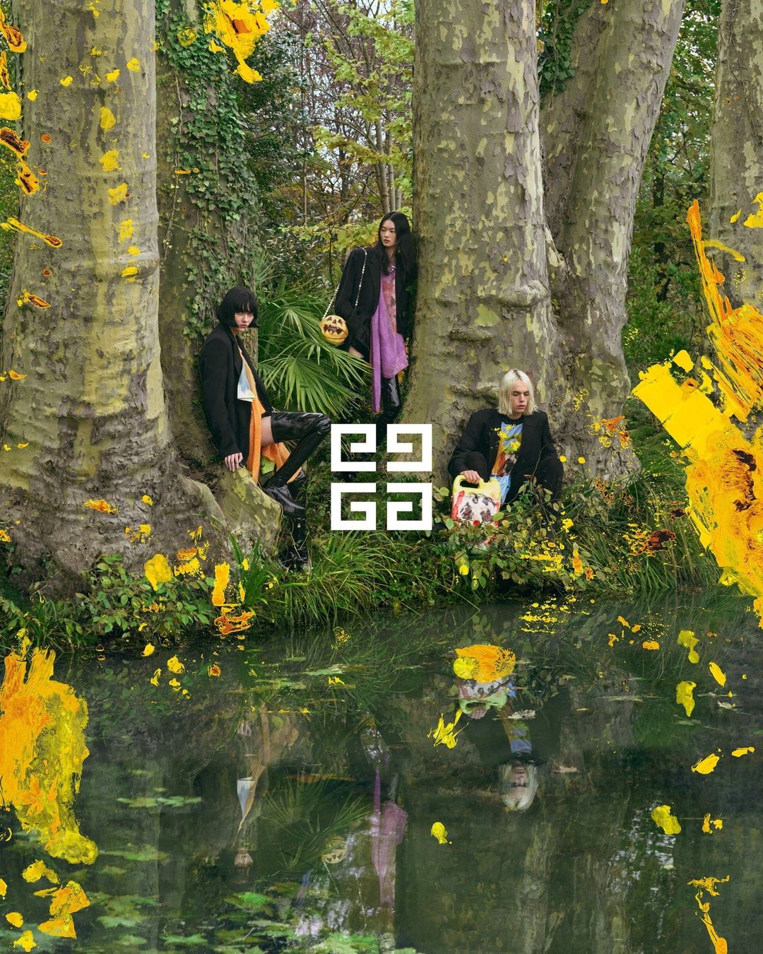 Three people in a wooded area with a pond, modelling black clothing for a fashion advertisement, featuring the Givenchy logo.