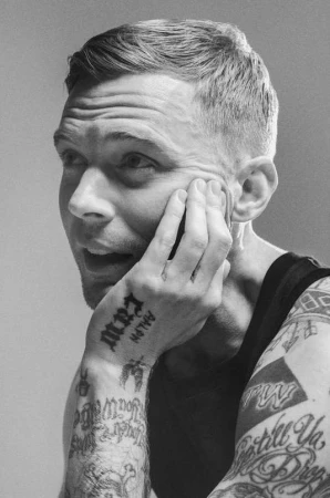 Black and white portrait of a tattooed man with short hair resting his hand on his cheek, photographed by Heji Shin.