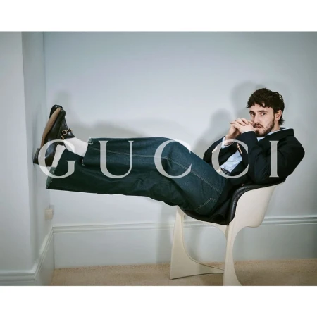 Man in dark blazer and jeans seated in a white chair with legs propped horizontally against a wall, shot by Heji Shin.