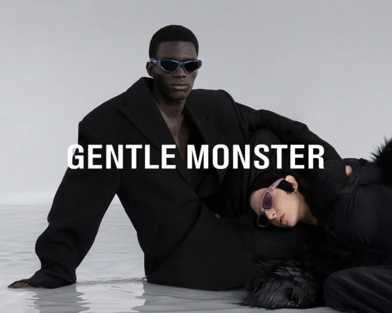 Two fashion models, one lying down, and the other sitting in a black blazer, wear trendy sunglasses in a studio shot.