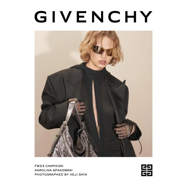 Fashion editorial featuring a model in a black blazer and sunglasses holding a metallic silver handbag in an indoor studio setting.