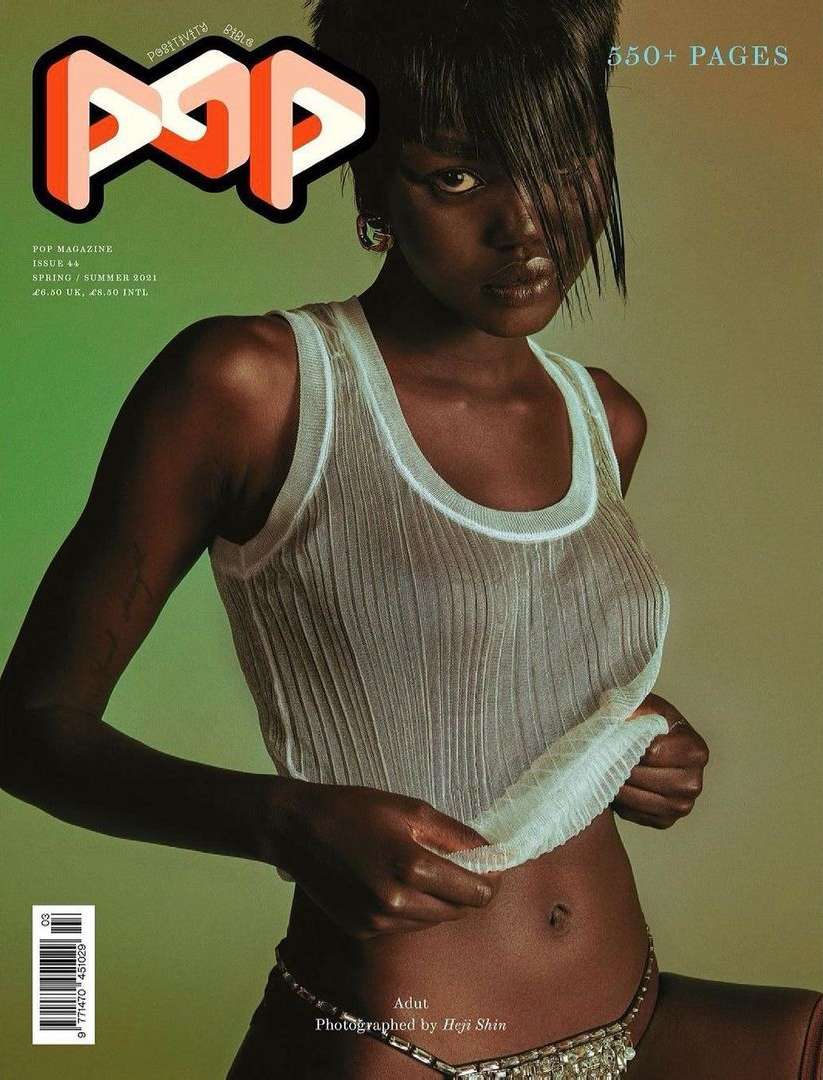 Magazine cover featuring a dark-skinned model wearing a semi-sheer top and jeweled belt, posing in front of a gradient background.