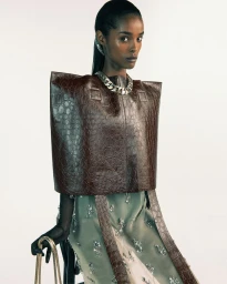 Black woman wearing a structured brown embossed leather top and sheer embellished dress against a seamless white background.