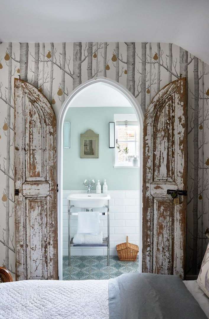 Bathroom with antique white doors, white washbasin, subway tile, and nature-themed wallpaper in an indoor setting.