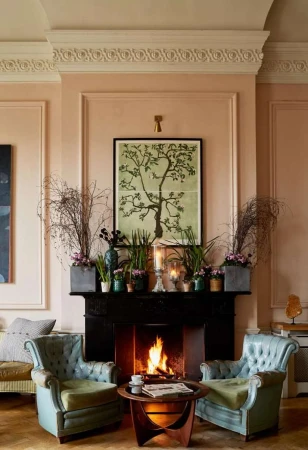Living room interior featuring a black fireplace with a burning fire, flanked by two blue armchairs and decorated with plants and artwork.