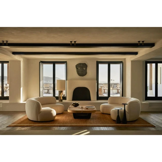 Living room interior featuring two curved sofas, a central coffee table, fireplace, and large windows with a view of a coastal landscape.