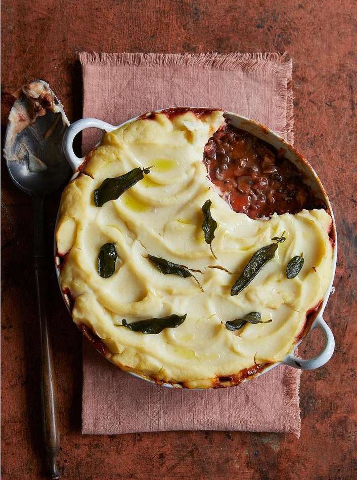 Overhead shot of shepherd's pie with mashed potato topping, decorated with sage leaves, next to a spoon and pink linen cloth.
