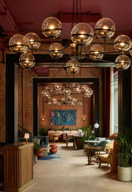 Lobby interior showcasing a modern chandelier above a reception area with lounge seating, tables, plants, and a blue abstract painting.