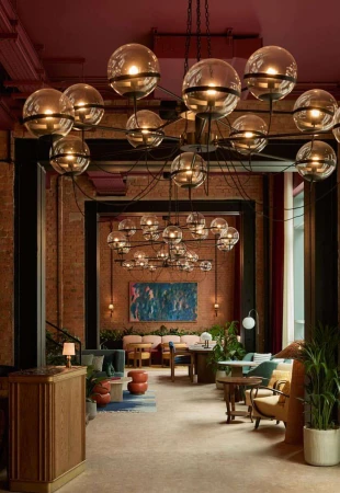 Lobby interior showcasing a modern chandelier above a reception area with lounge seating, tables, plants, and a blue abstract painting.