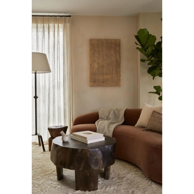 Living room interior with a brown curved sofa, a unique wooden coffee table, a floor lamp, and neutral decor, creating a warm, inviting space.