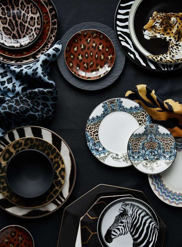 Overhead shot featuring a variety of decorative plates with animal prints and patterned designs, arranged on a dark surface with fabric accents.