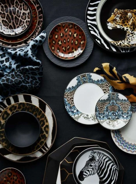 Overhead shot featuring a variety of decorative plates with animal prints and patterned designs, arranged on a dark surface with fabric accents.