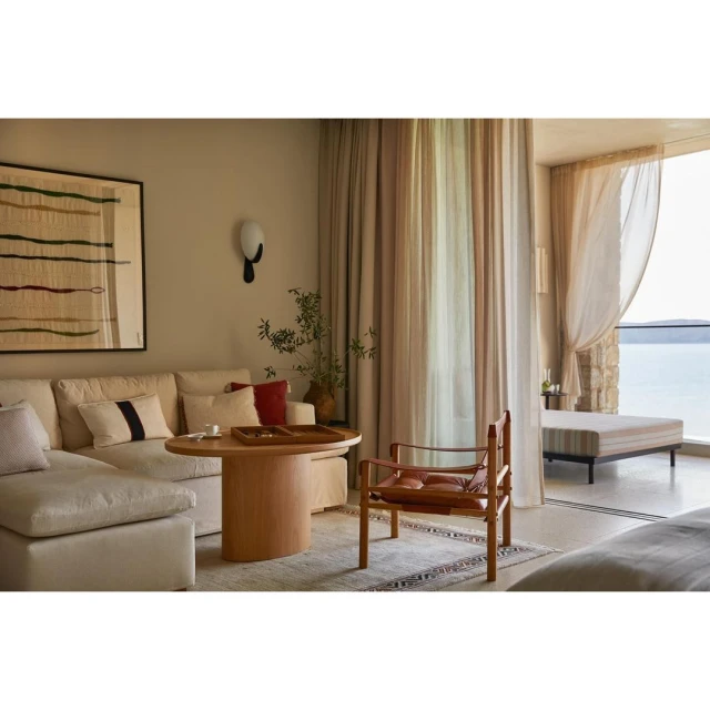Contemporary living room with a beige sofa, wooden table, chair, and view of the ocean through a window, creating a serene atmosphere.