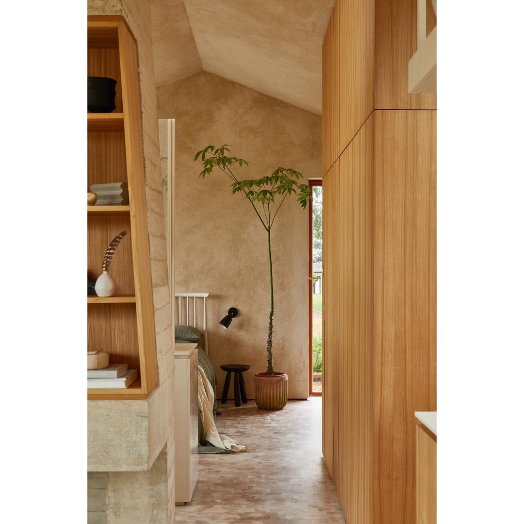 Interior view of a bedroom with natural wood features, including a potted plant, a bed with green bedding, and exposed concrete wall.