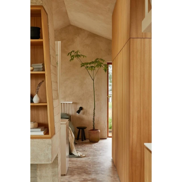 Interior view of a bedroom with natural wood features, including a potted plant, a bed with green bedding, and exposed concrete wall.