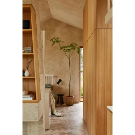 Interior view of a bedroom with natural wood features, including a potted plant, a bed with green bedding, and exposed concrete wall.