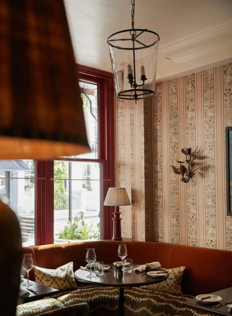 Restaurant interior featuring a table set for dining, surrounded by banquette seating and illuminated by a hanging lantern light fixture.