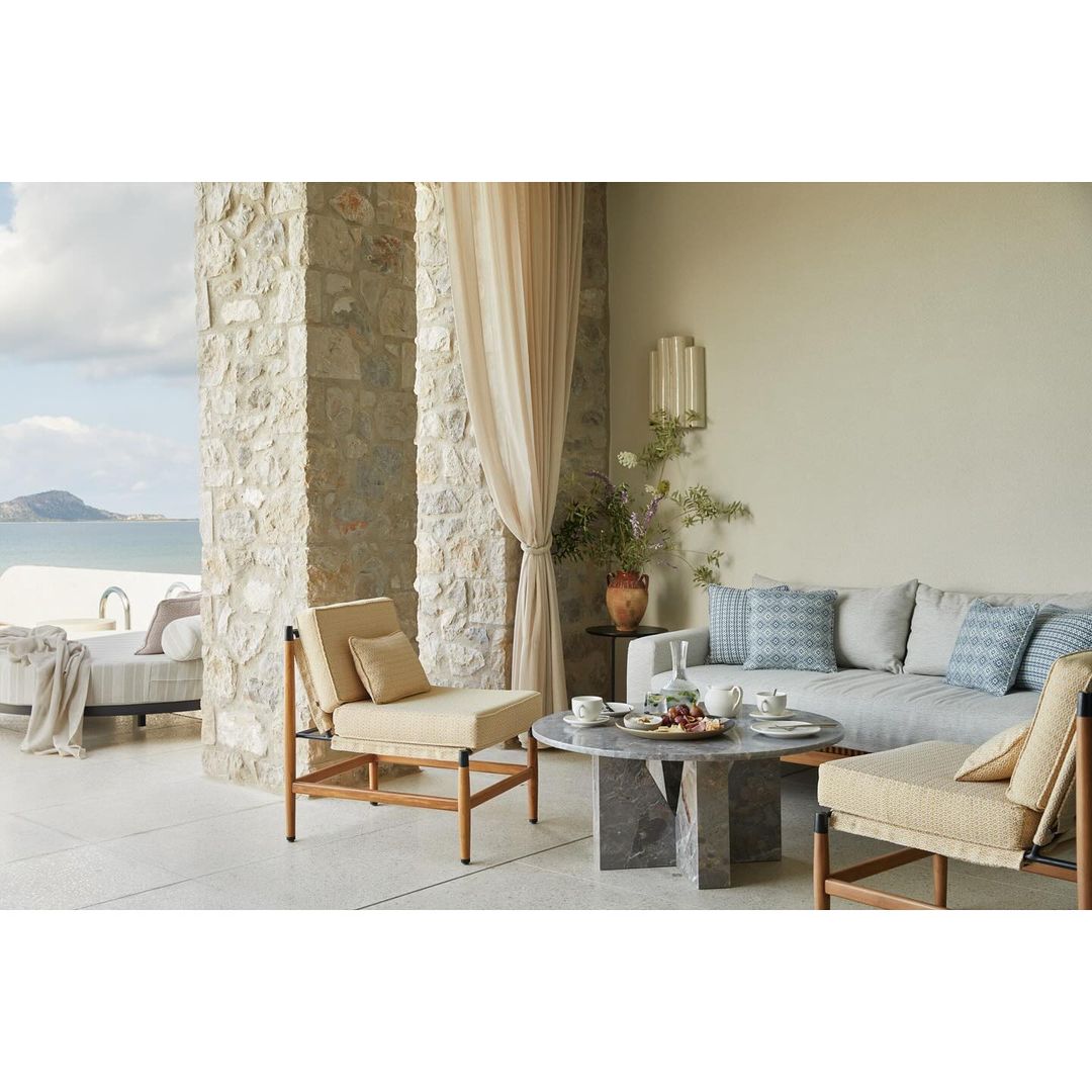 Outdoor seating area with beige lounge chairs and sofa on a patio, offering ocean views in the distance. Stylish outdoor furniture.