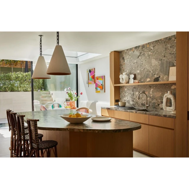 Modern kitchen interior featuring a central island with lemons, hanging pendant lights, light wood cabinets, and abstract art pieces.