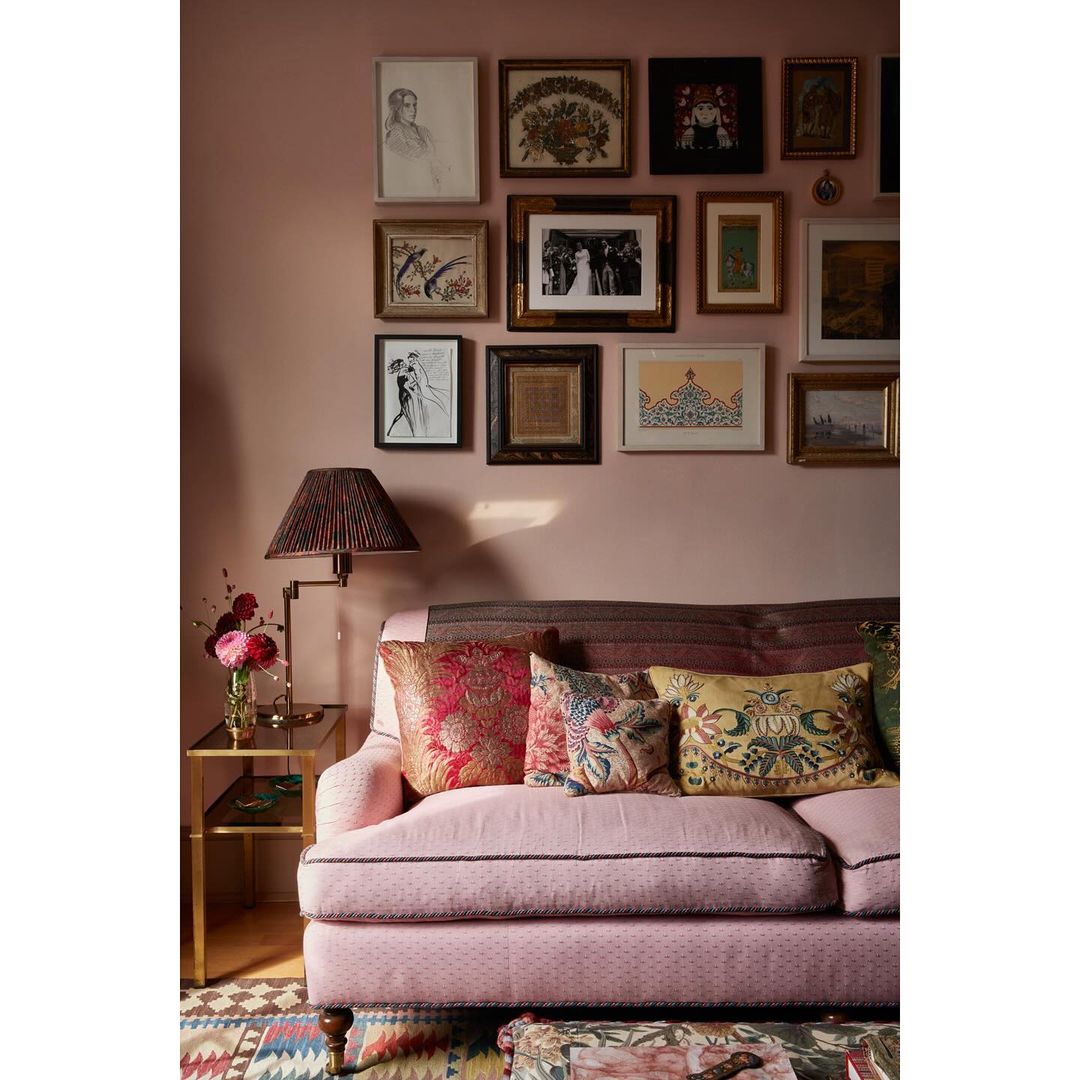 Pink couch with decorative pillows in a room with a gallery wall featuring various framed artworks above the sofa, plus a side table.