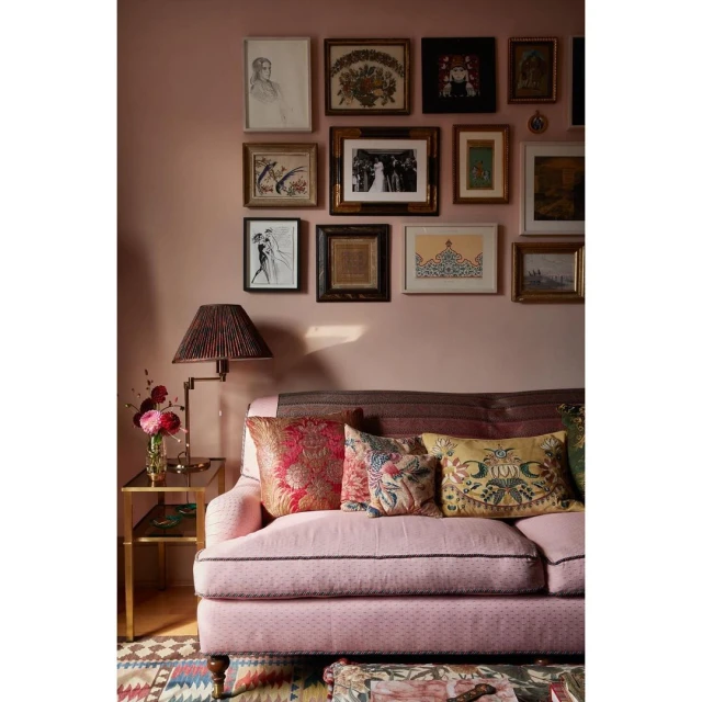 Pink couch with decorative pillows in a room with a gallery wall featuring various framed artworks above the sofa, plus a side table.