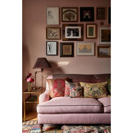 Pink couch with decorative pillows in a room with a gallery wall featuring various framed artworks above the sofa, plus a side table.