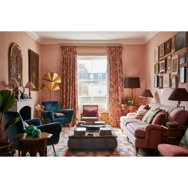 Living room interior showcasing floral curtains, pink walls, armchairs, and a patterned rug, creating a warm and inviting atmosphere.