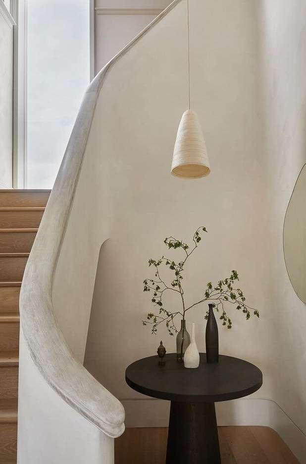 Interior design shot of a stairway and round table with bottles and foliage, illuminated by a cone-shaped pendant light.