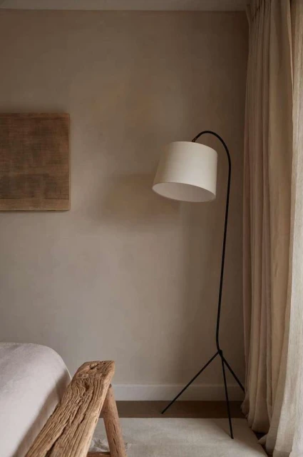 Minimalist interior with a modern arc floor lamp, wood accent table, neutral color palette, and a serene, comfortable bedroom environment.