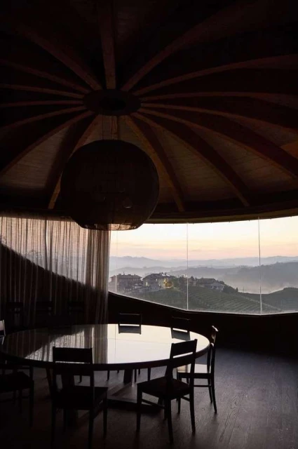 Interior dining room with a round table and chairs looking out a window with a view of rolling hills at dusk.