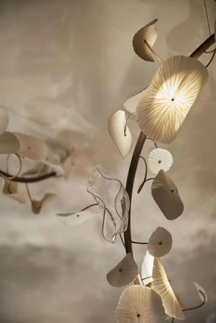 A contemporary lighting fixture features organic forms and textures, casting a soft, diffused glow in a blurred indoor setting.