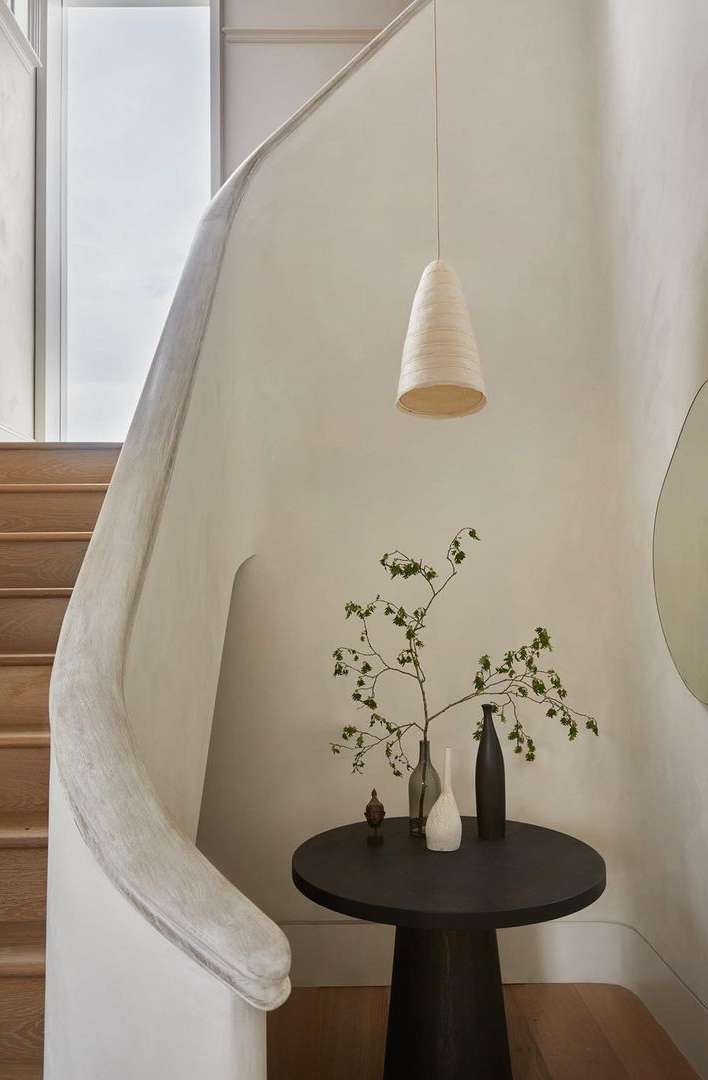 Indoor entryway featuring a modern pendant light, round table with vases, and a staircase, creating a minimalist and elegant design.