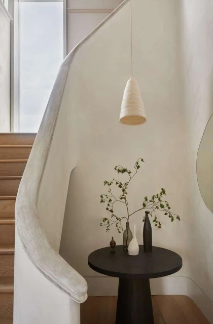 Indoor entryway featuring a modern pendant light, round table with vases, and a staircase, creating a minimalist and elegant design.