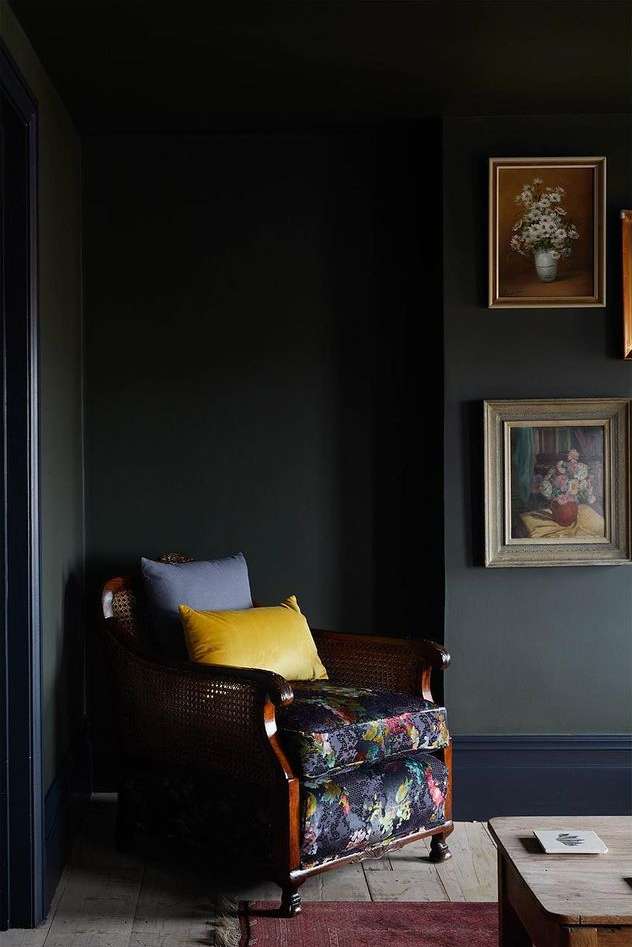 Interior design featuring a dark-green living room with a patterned armchair, throw pillows, framed wall art, and wooden floors.