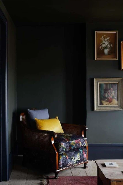 Interior design featuring a dark-green living room with a patterned armchair, throw pillows, framed wall art, and wooden floors.